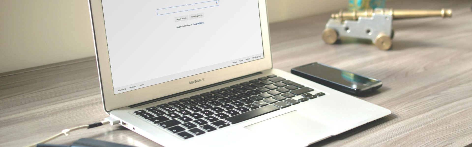 A neat workspace featuring a laptop displaying Google search, a smartphone, and a notebook on a wooden desk.